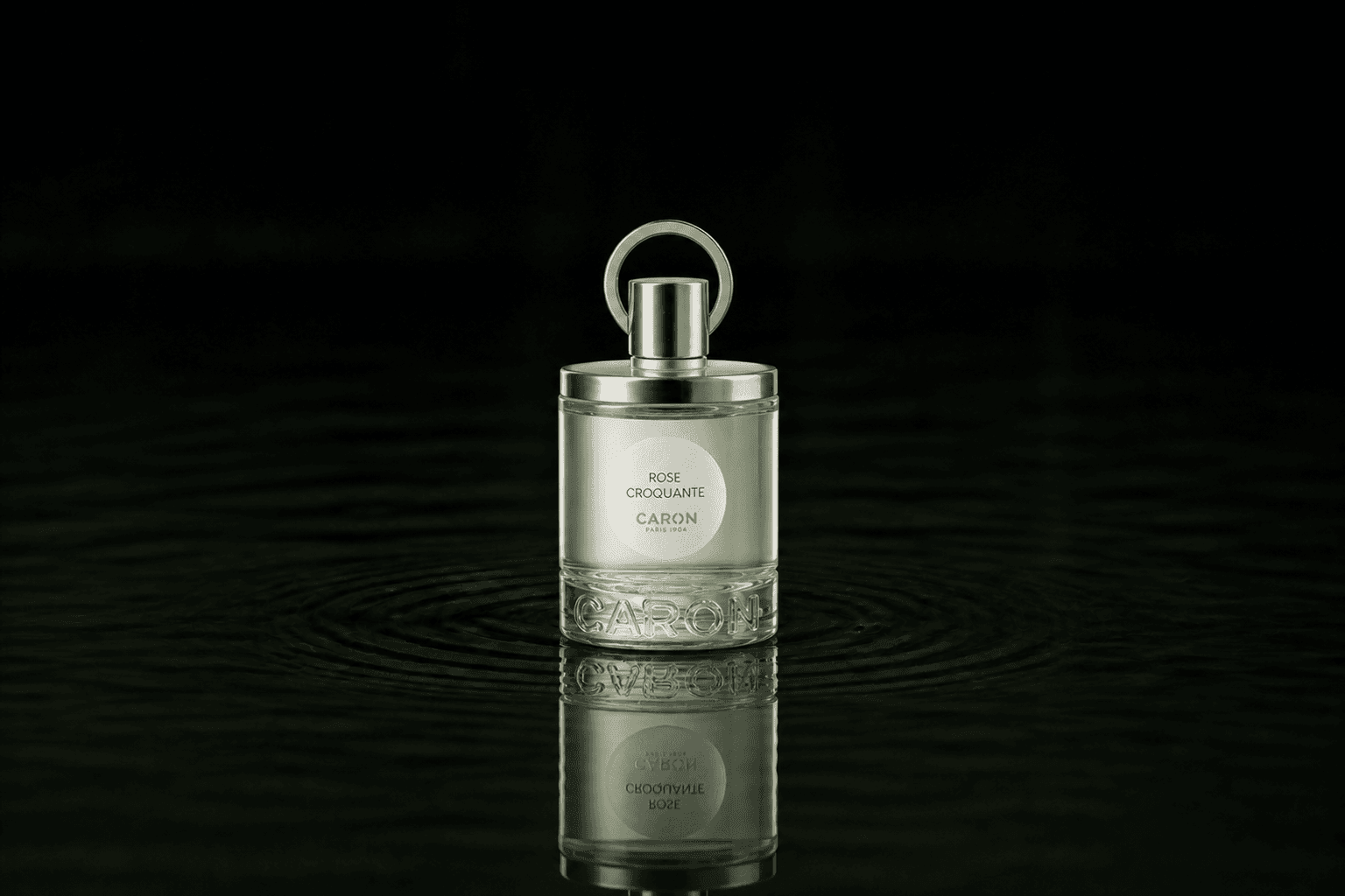 Caron Rose Croquante fragrance bottle floating above dark water
