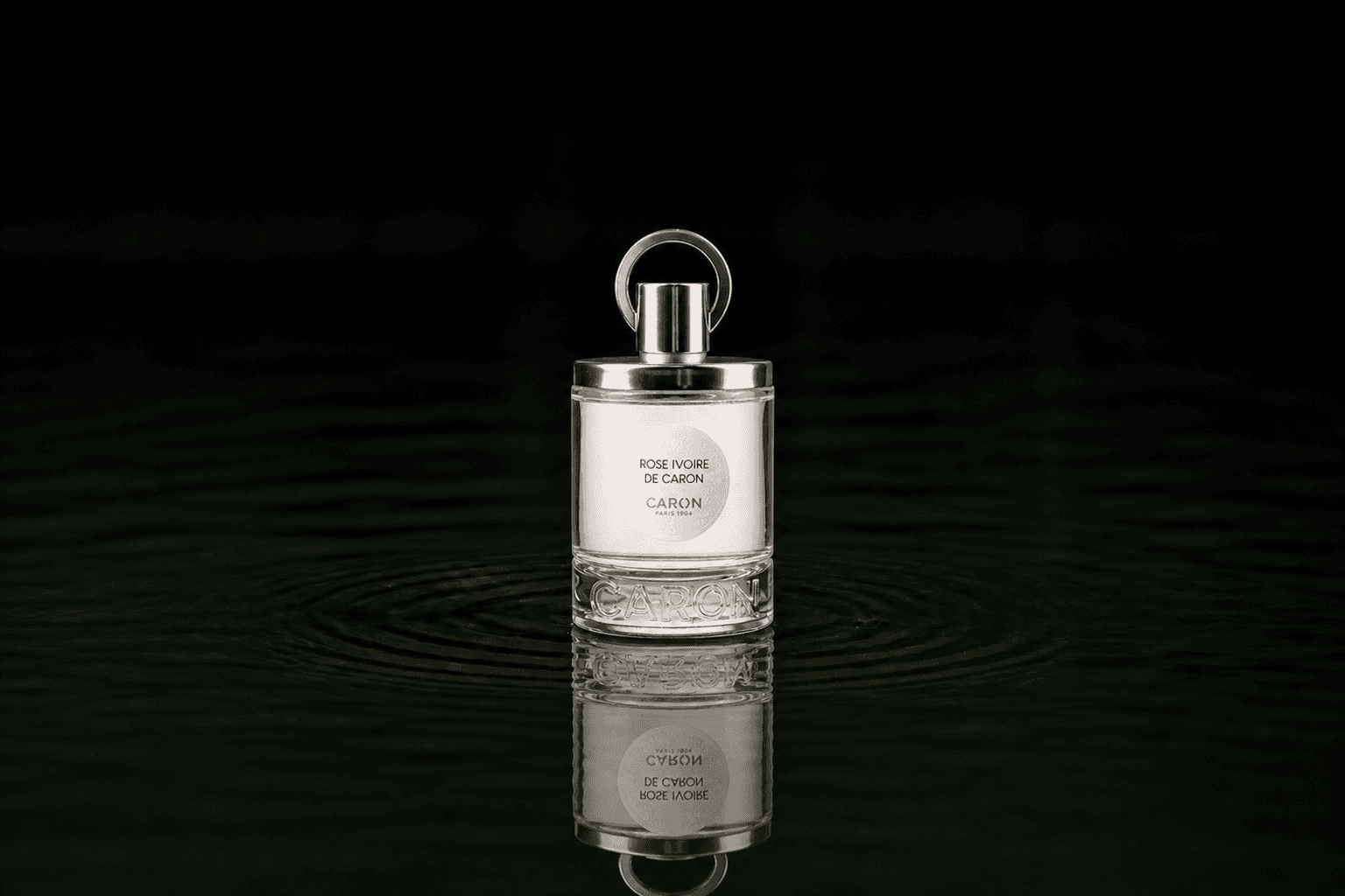 Caron Rose Ivoire De Caron fragrance bottle floating above dark water