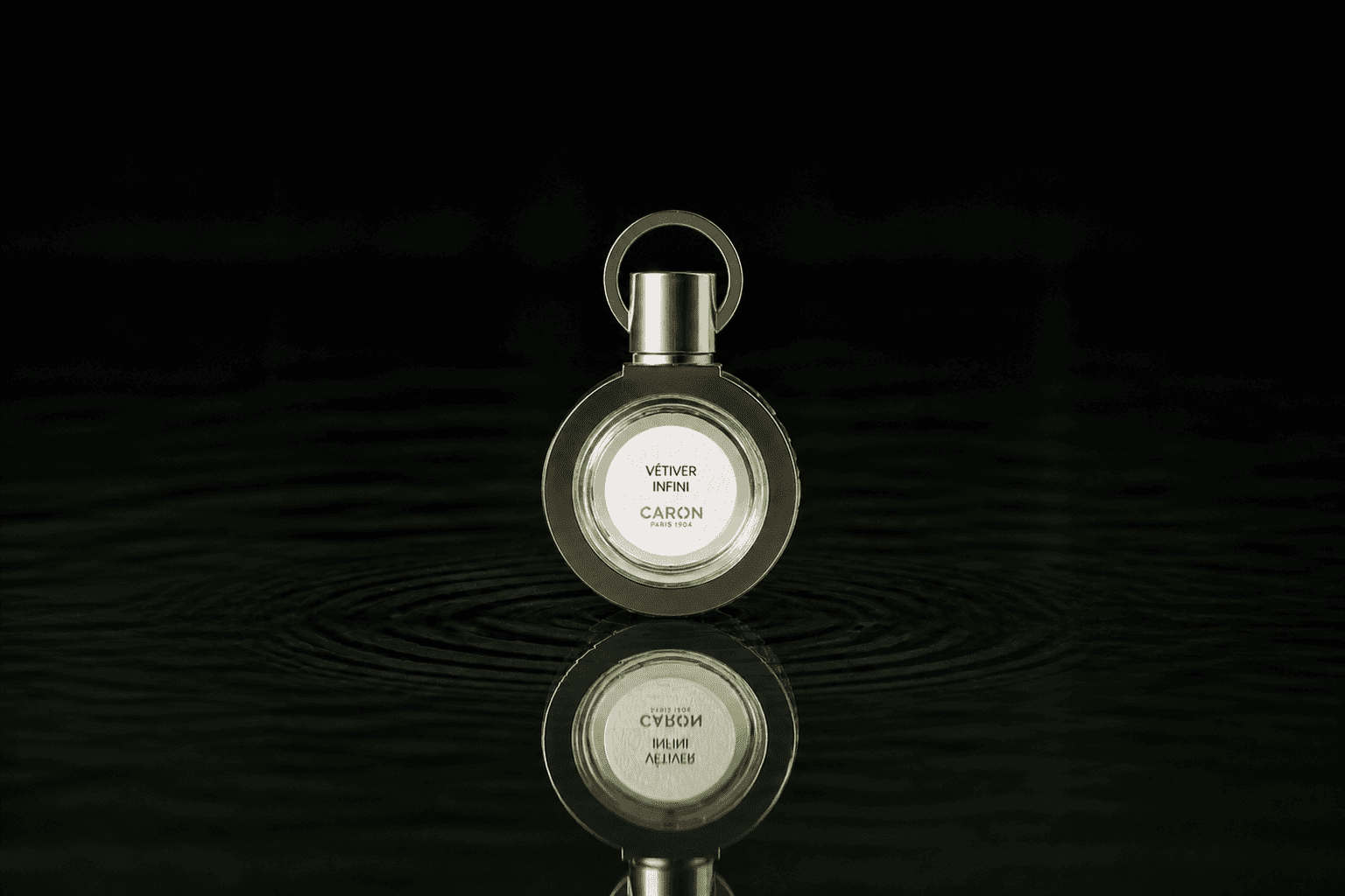 Caron Vetiver Infini Refillable fragrance bottle floating above dark water