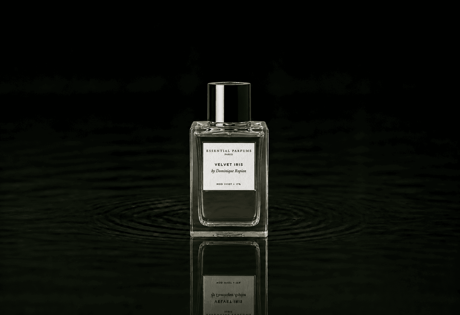 Essential Parfums Velvet Iris fragrance bottle floating above dark water