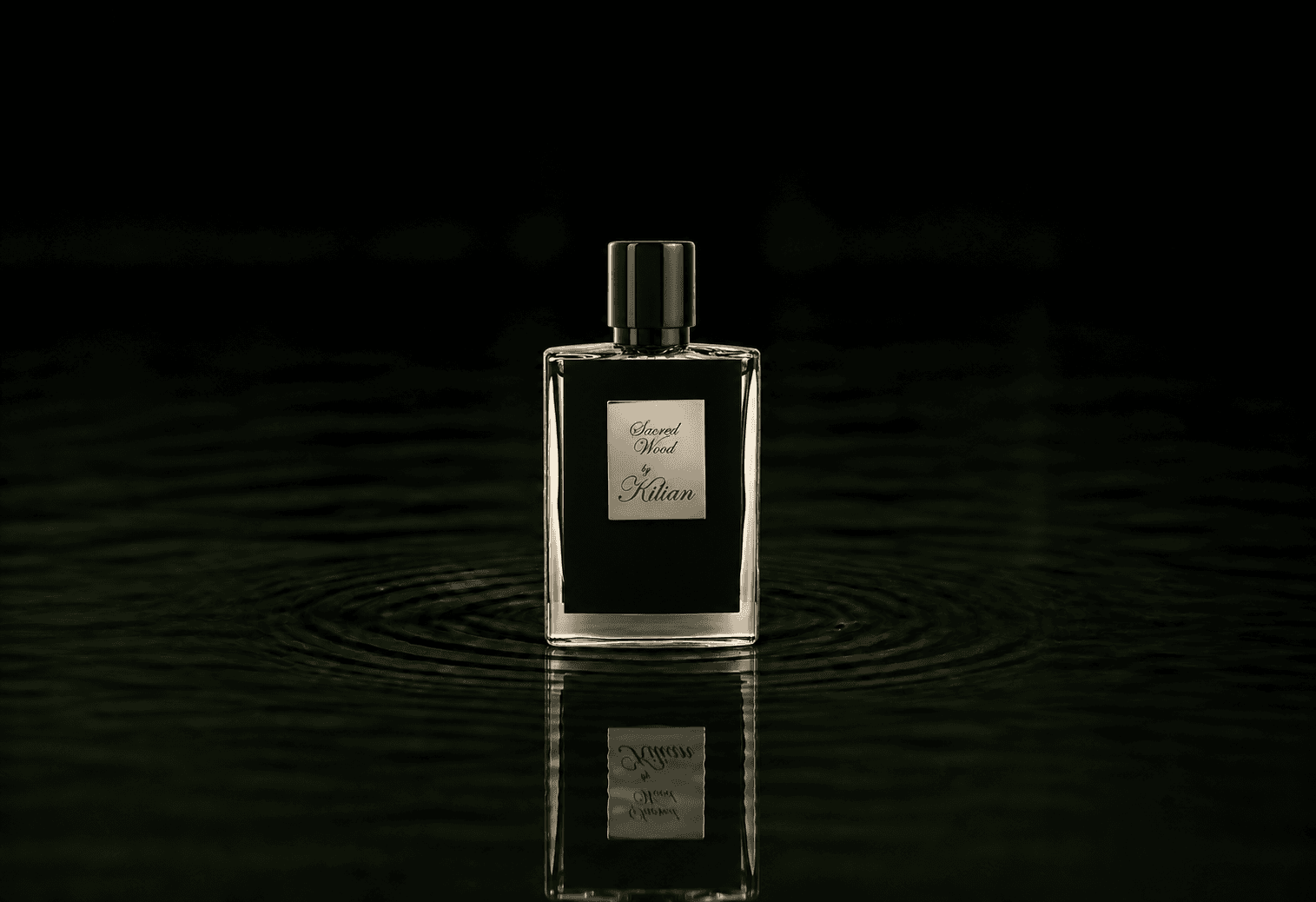 Kilian Sacred Wood fragrance bottle floating above dark water